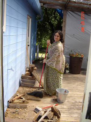 Madhurapriya Didi cleans the flower porch and firewood area.