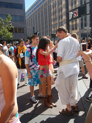 Jaya Ram Prabhu chanting in the background and in the foreground, Kesavananda Prabhu receives a sticker from one of the festival attendees.