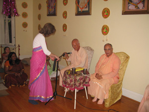 Jivana Didi sets up the microphone for the guest speaker,  Sripad Ashram Maharaj, who is accompanied by Sripad Janardan Maharaj. 